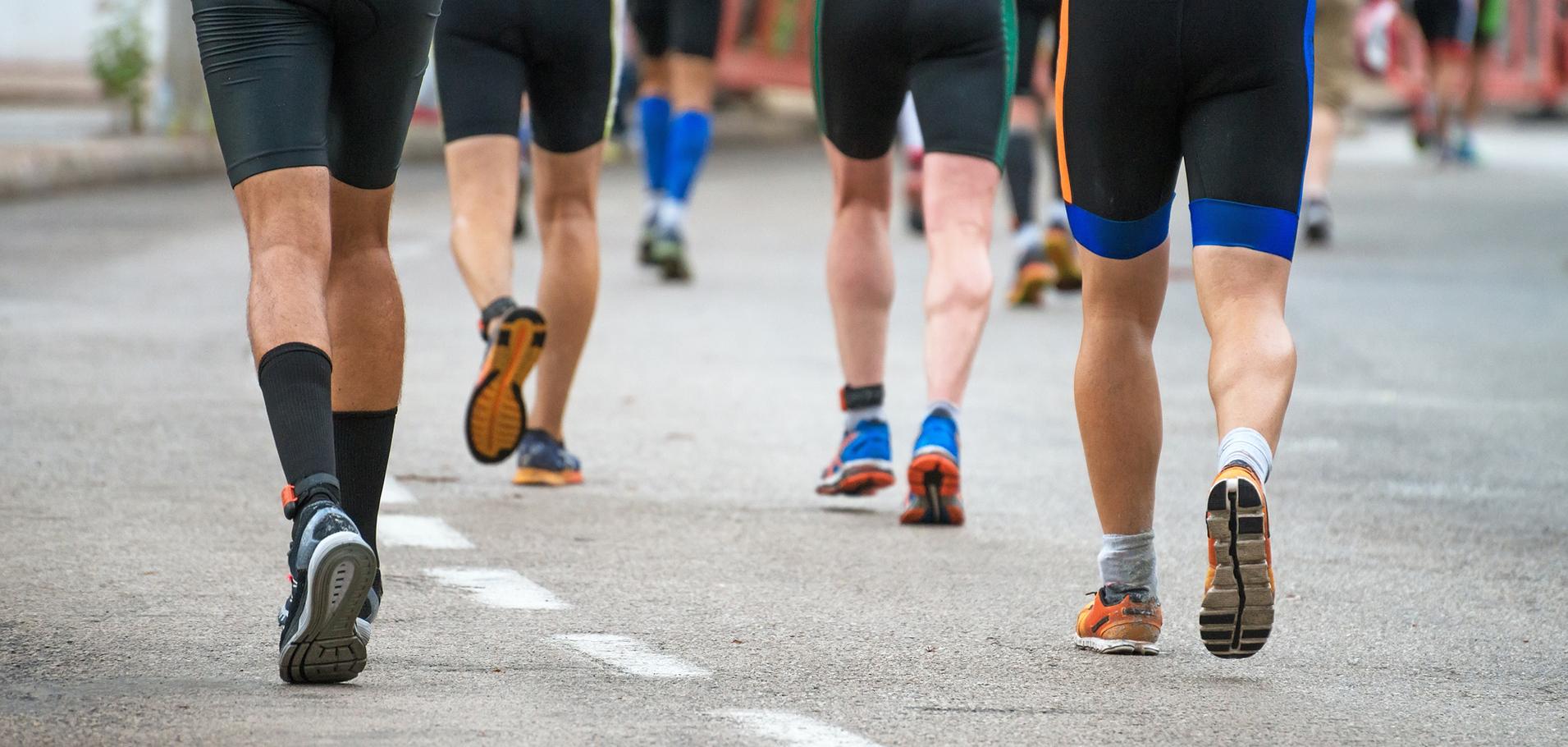 Gruppe von Männern in Sportkleidung joggt auf einer asphaltieren Straße, während sie dem Rennen folgen.