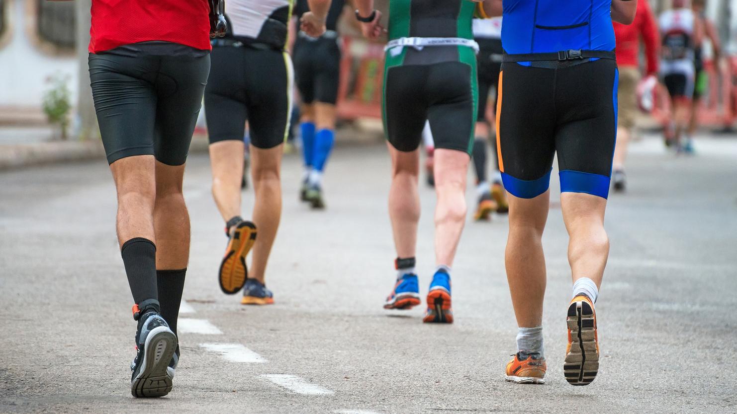 Gruppe von Männern in Sportkleidung joggt auf einer asphaltieren Straße, während sie dem Rennen folgen.